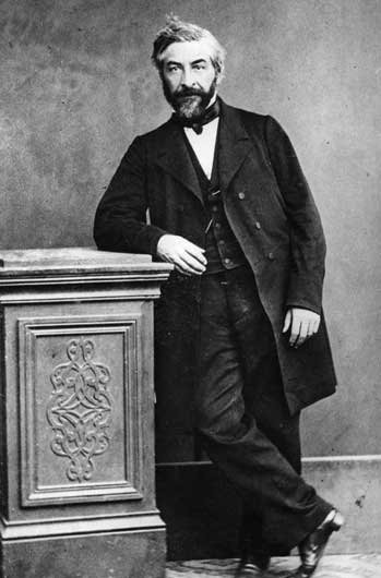 black and white photo of a man standing next to a desk
