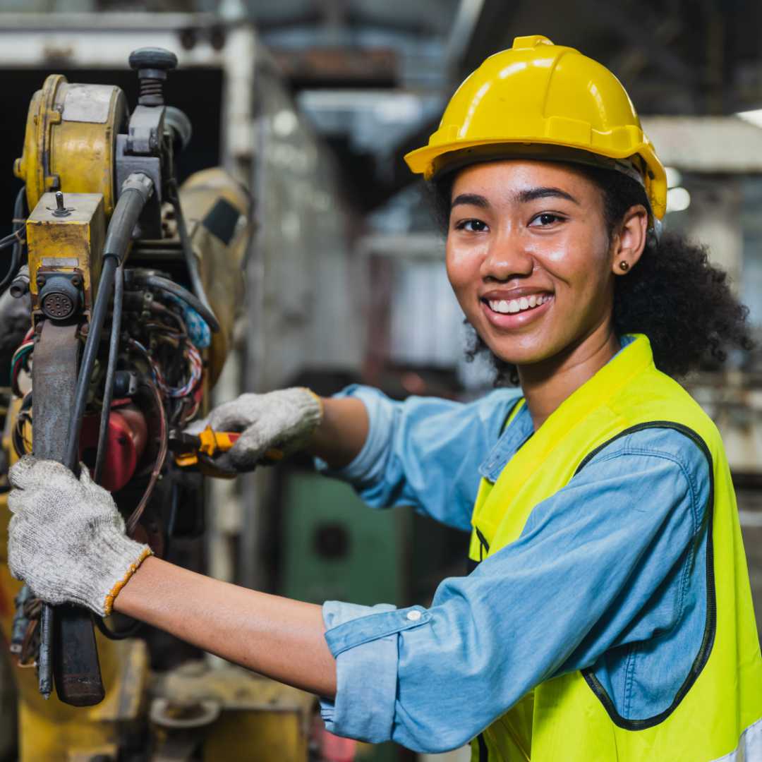woman in a hard hat and safety vest working on a machine